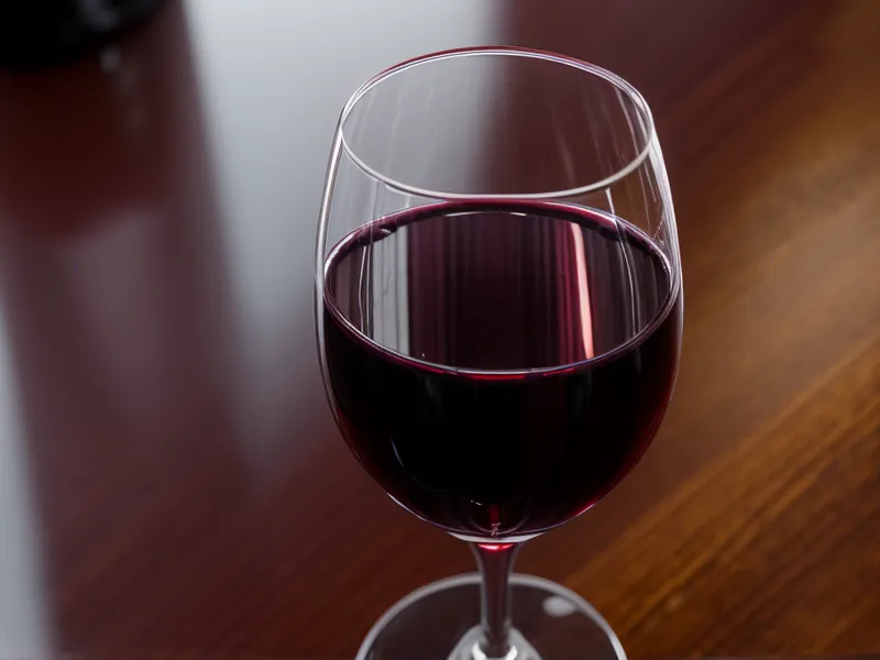 A glass of red wine next to a laptop in a dimly lit office.